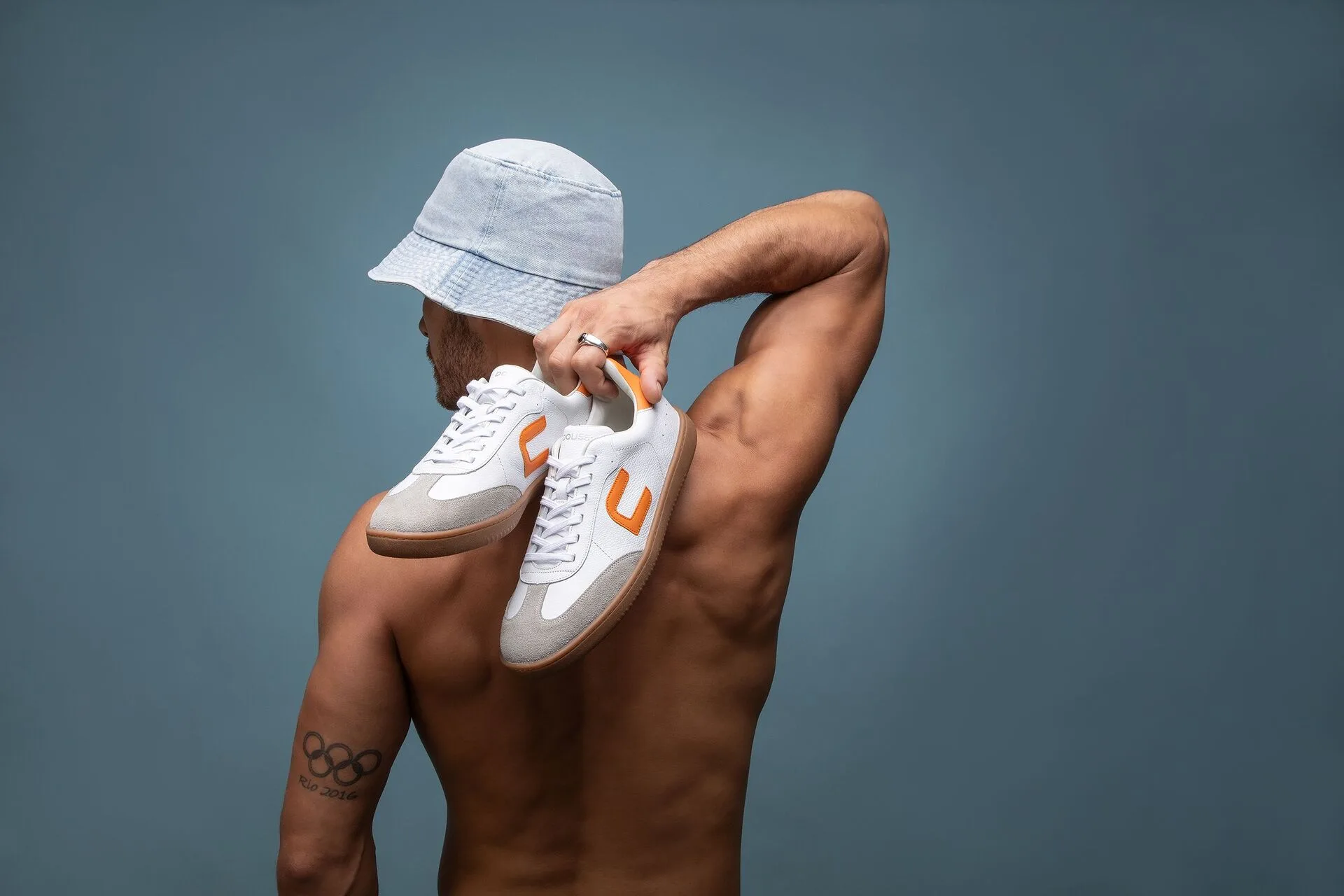 homem de costas sem camisa usando um chápeu jeans azul claro segurando um par do tênis douss one citrus