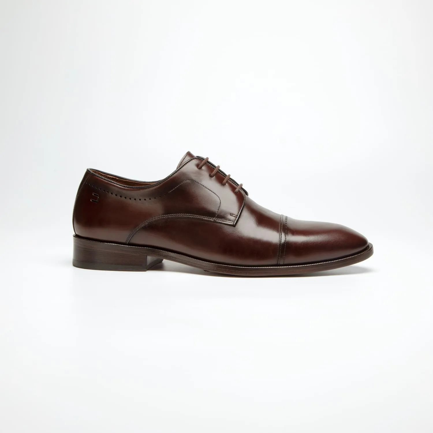 pé do sapato social douss spiga estilo derby, couro marrom escuro com furos como detalhes, cadarços finos na cor marrom escura, solado e salto na cor marrom escura visto de lado