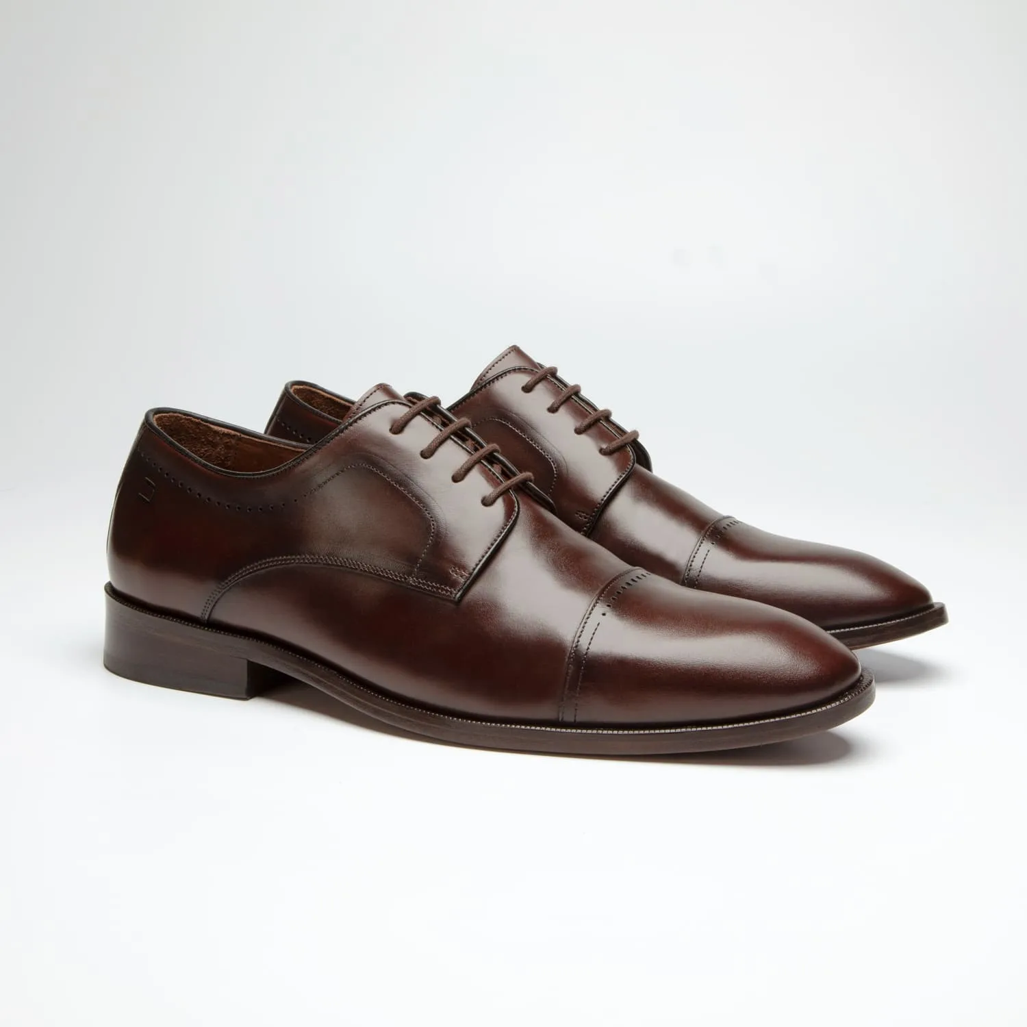 par do sapato social douss spiga estilo derby, couro marrom escuro com furos como detalhes, cadarços finos na cor marrom escura, solado e salto na cor marrom escura visto de frente na diagonal